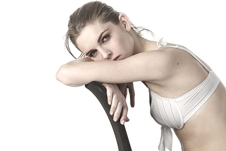 woman wearing white brassiere leaning on black chair's backrest thumbnail