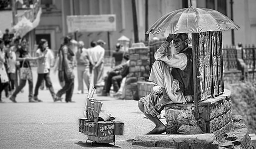 grayscale photo of man sitting under umbrella thumbnail