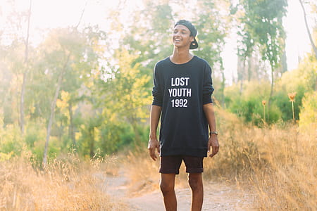 smiling man wearing black long-sleeved shirt standing between dried grass field thumbnail