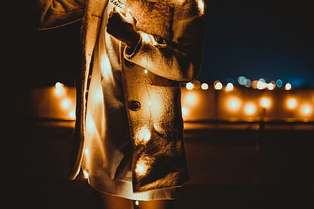 person in brown coat holding lighted brown string lights thumbnail
