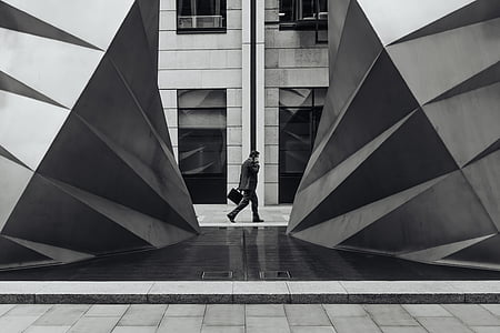 grayscale photo of man walking beside building thumbnail