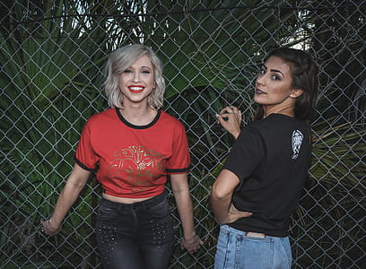 Two Woman in Black and Red Dress Standing Near Fence thumbnail