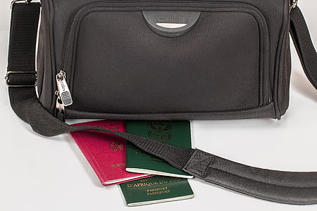 black crossbody bag and three passports on white surface thumbnail