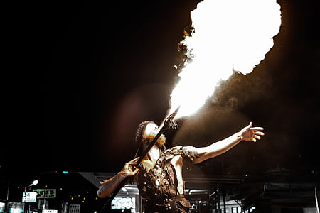 man holding stick while blowing fire during nighttime thumbnail