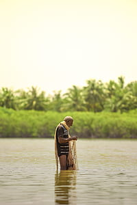 man standing in body of water while holding fishing net thumbnail