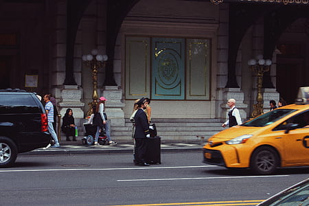 man in black formal suit standing in middle of road near yellow car thumbnail