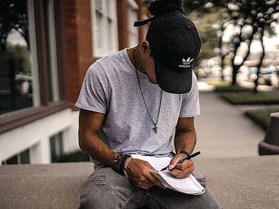 man writing on book near building thumbnail