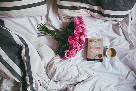 pink rose flower bouquet beside Me Before You by Jojo Moyes book and white ceramic mug on white and black bedspread thumbnail