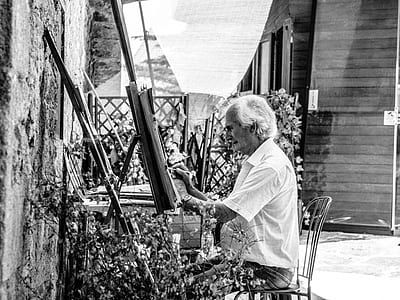 grayscale photo of man sitting on chair while painting thumbnail