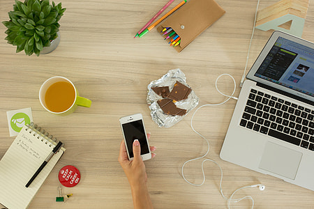 photo of person holding smartphone surrounded with laptop, chocolates, pens, notes, and cup with coffee thumbnail