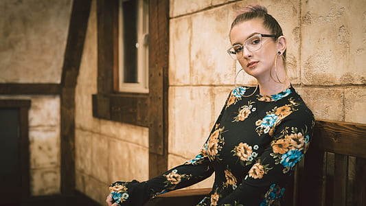 woman wearing black framed eyeglasses and black and yellow floral long-sleeved crew-neck dress sitting on brown wooden chair thumbnail