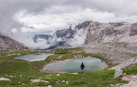 man standing on green mountain facing towards body of water thumbnail