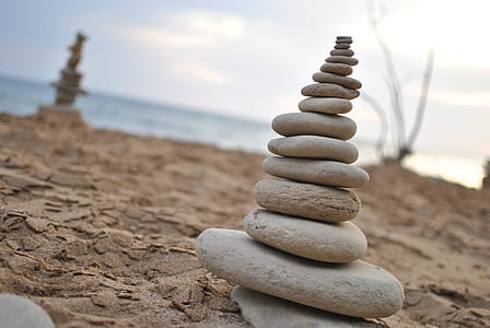 stacked stones on gray sand near body of water under white clouds during daytime thumbnail