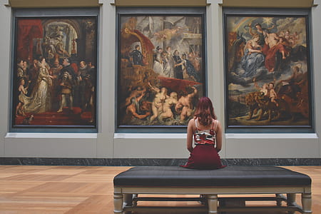 woman sitting on chair facing three assorted paintings mounted on wall thumbnail