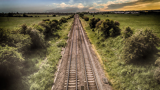 aerial view of black train rail between green trees under cloudy sky thumbnail
