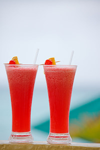 two clear curved drinking glasses filled with red liquid with a slice of lemon placed on wooden surface thumbnail
