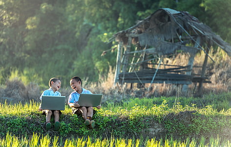 two toddlers sitting on grass field while holding gray laptops thumbnail
