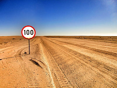 white, black, and red 100-printed signage on desert during daytime thumbnail