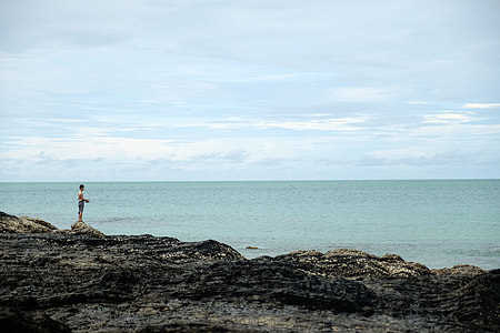 man standing on gray rock formation beside sea thumbnail