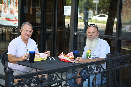 two man sitting on metal armchair while eating on table thumbnail