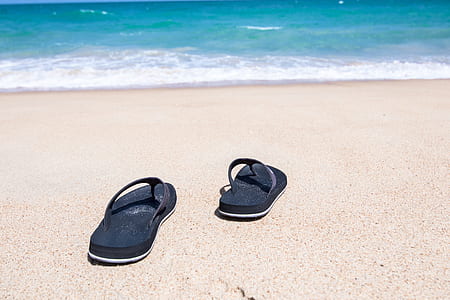 pair of black flip-flops on brown sand along seashore thumbnail