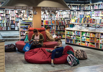 four people sitting in red cushion and chairs while reading book inside library thumbnail