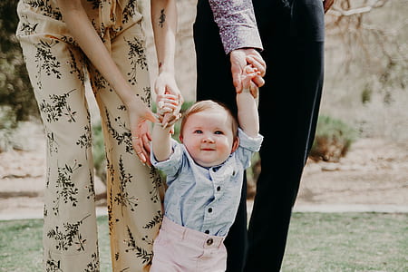 baby holding hands between two person walking on green grass thumbnail