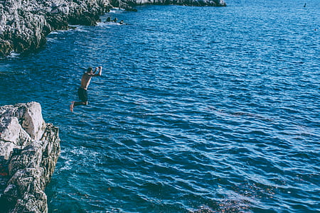 person jumped-off gray cliff towards body of water thumbnail