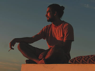 man having cigarette on edge of wall near pillow during golden hour thumbnail
