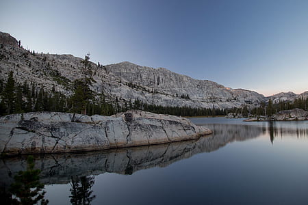 body of water surrounded by mountains under blue sky thumbnail