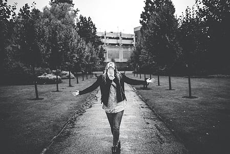grayscale photo of woman walking on pathway surrounded by trees thumbnail