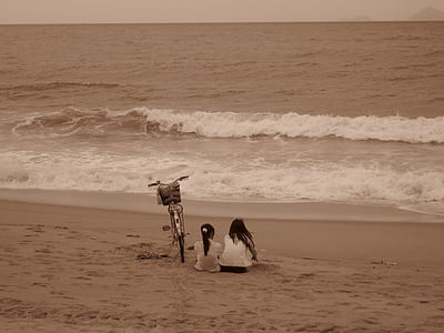 two girls sitting on sands near shoreline thumbnail