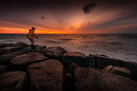 man standing on rock while fishing thumbnail