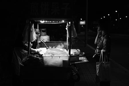 grayscale photo of woman front of food cart thumbnail