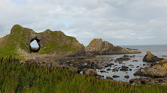 brown and green rock formations beside body of water thumbnail