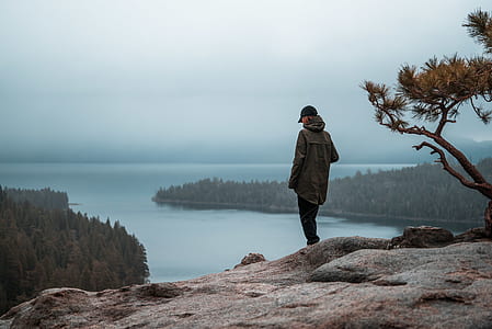 woman standing on edge of cliff with body of water nearby thumbnail