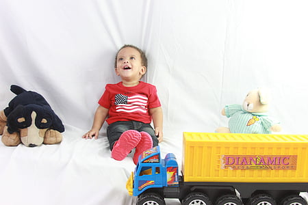 boy in red crew-neck t-shirt sitting beside black and brown dog plush toy thumbnail