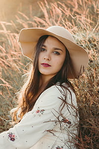 woman wearing sunhat sitting surrounded with brown grass thumbnail
