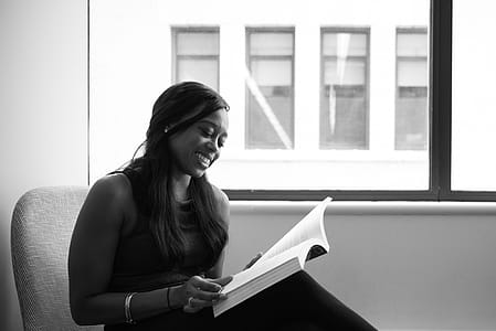 Grayscale Photo of Smiling Woman Reading Book thumbnail