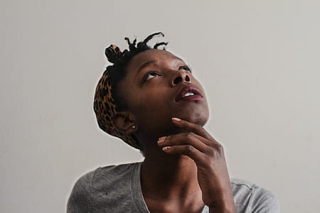 woman wearing brown leopard print headscarf and gray shirt looking up with her left hand on her chin thumbnail