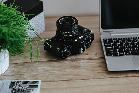 Black-and-white photos with a silver laptop, a smartphone, car keys, pencils and a camera thumbnail