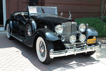 classic black convertible coupe parked beside brown building thumbnail