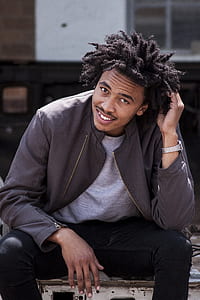 man smiling and sitting while touching his hair during day thumbnail