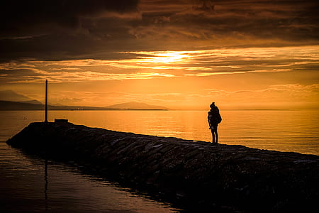 man standing near water during golden hour thumbnail