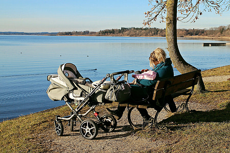 woman sitting on bench with stroller located near the body of water thumbnail