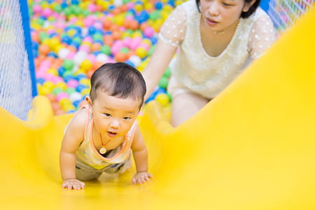 woman wearing white shirt with baby crouching on plastic slide thumbnail