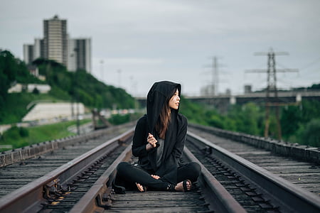woman wearing black zip-up hooded jacket sitting on train railway thumbnail
