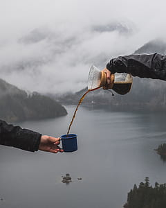 person pouring coffee into blue ceramic mug from glass pitcher thumbnail