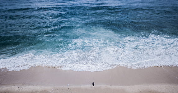 person standing on beach in front of wide body of water during daytime thumbnail