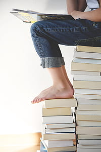 person wearing blue denim jeans while sitting on books thumbnail